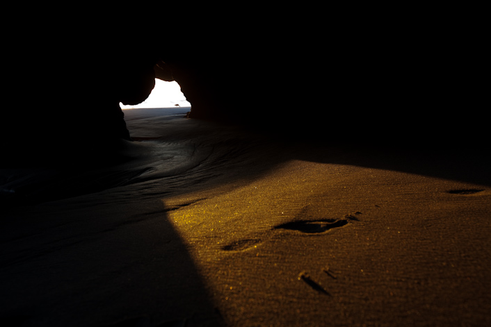 A golden footprint glistens in the sand inside a cave